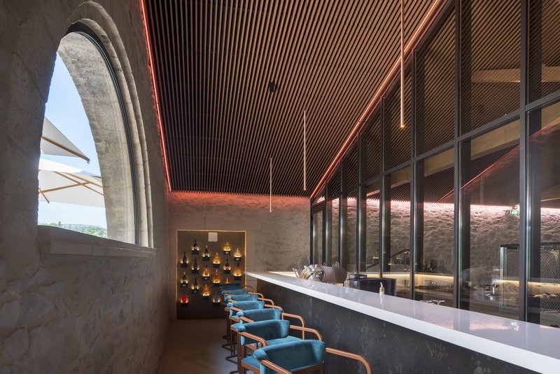Tasting bar with timber slat ceiling, arched stone window opening, and metal mesh wine storage behind glass