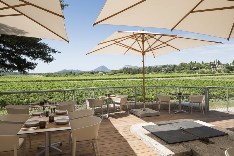 Outdoor timber deck terrace with fabric shade umbrellas overlooking vineyard rows and distant hills under blue sky