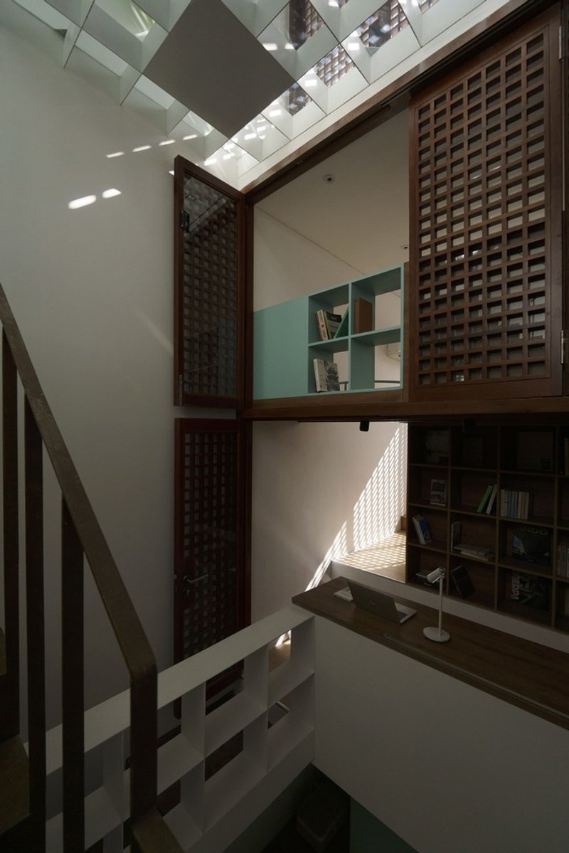 Interior courtyard with timber lattice screens and bookshelves beneath a geometric skylight casting angular shadows