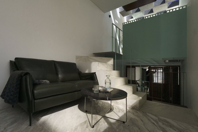 Sitting area with black leather sofa and marble clad stair illuminated by overhead skylight