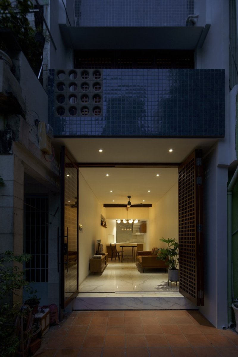 Street facade at dusk showing open glass wall revealing living room and tiled upper terrace with perforated screens