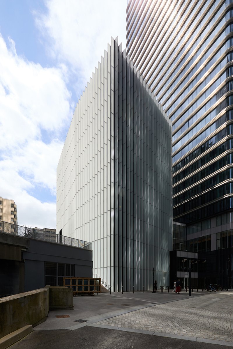 Vertical metal fin facade rising above the street level entrance under a cloudy sky