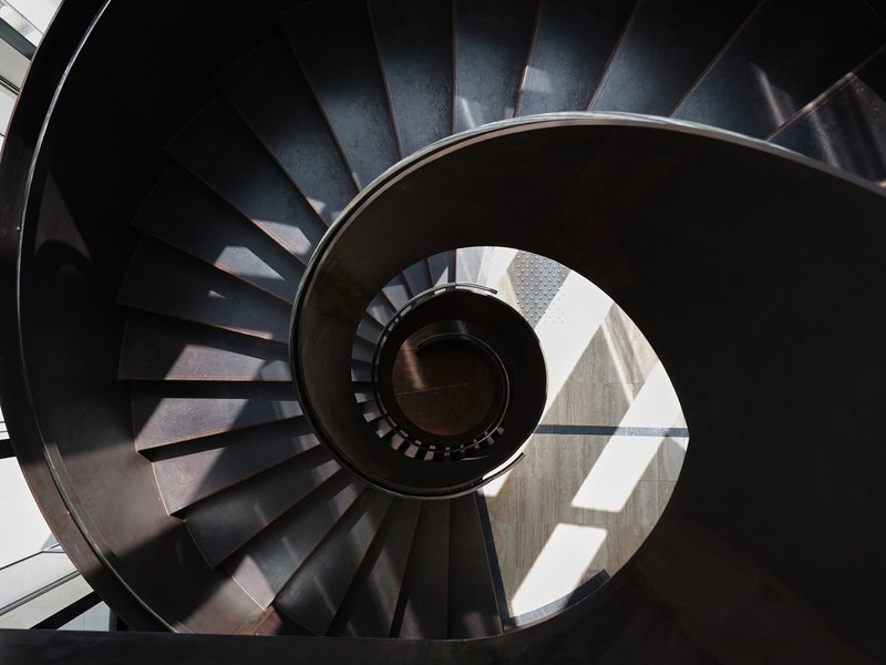 Top-down view of the spiral staircase with dark steel treads and sunlight illuminating the central void