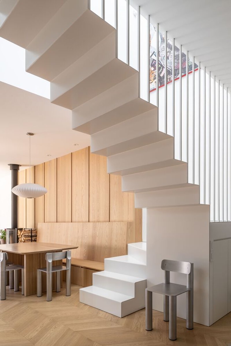 Floating white staircase with vertical slat balustrade filtering natural light from a clerestory window