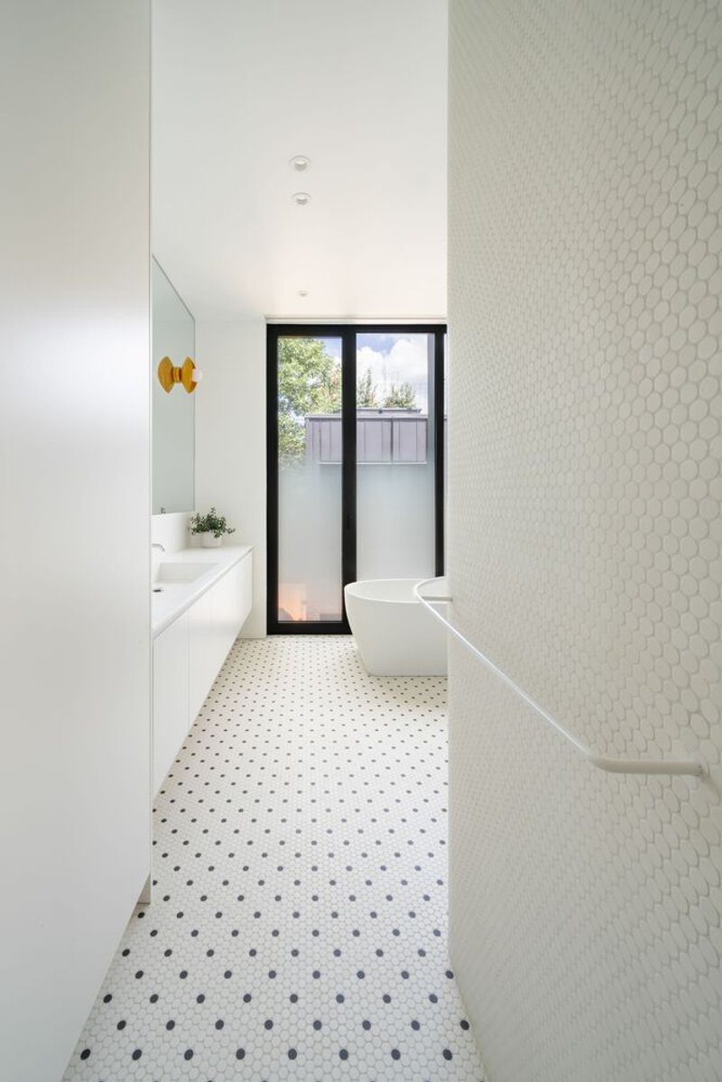 Bathroom with white hexagonal tile wall, terrazzo floor and black-framed glazed door to garden