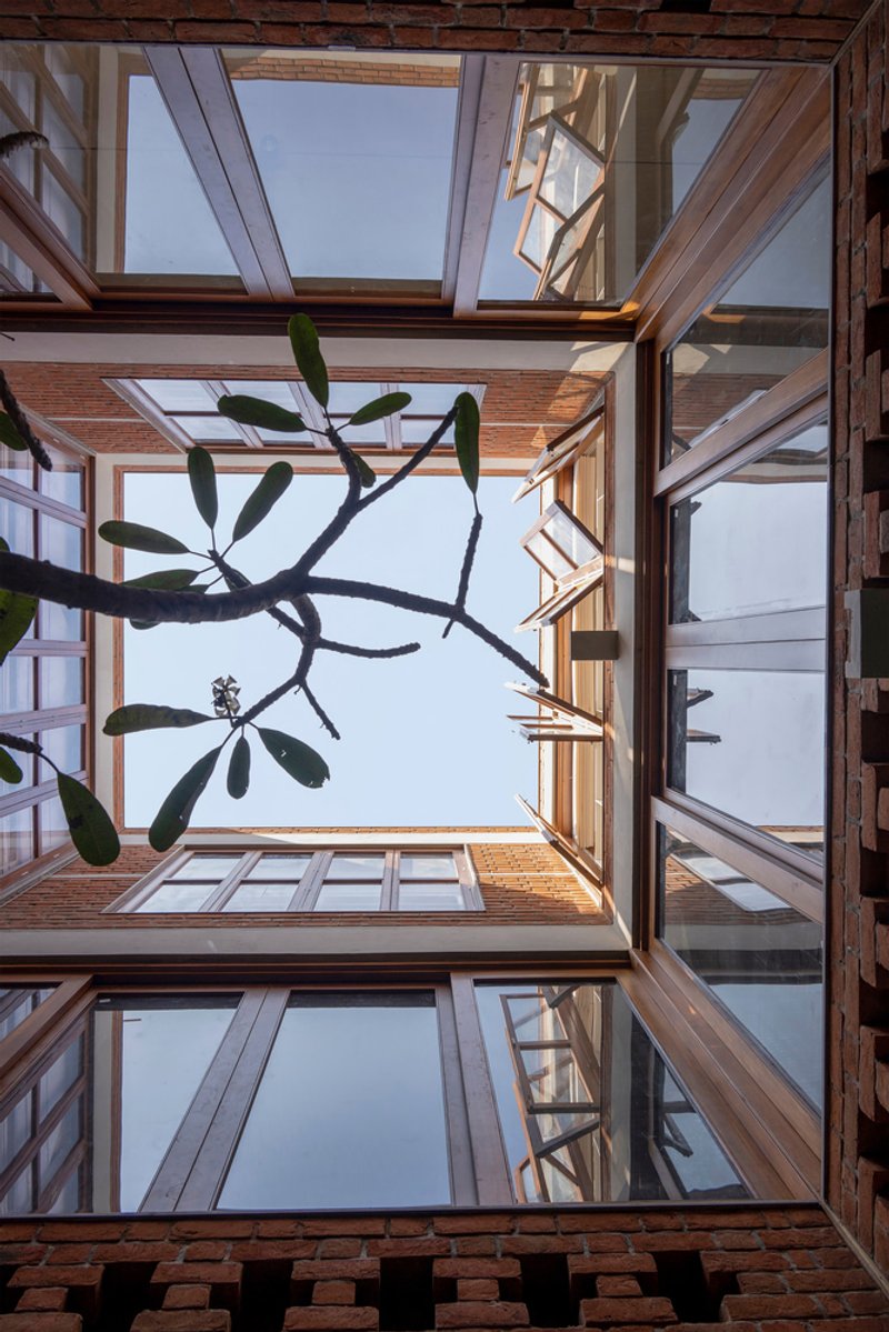 Looking up through the open courtyard with timber-framed balconies and a plumeria tree overhead