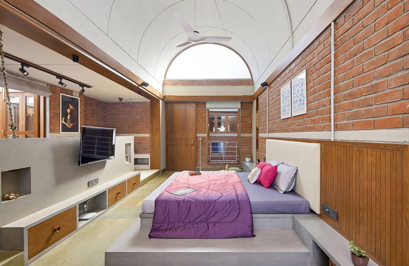 Bedroom with vaulted ceiling, exposed brick walls, timber paneling, and arched skylight overhead