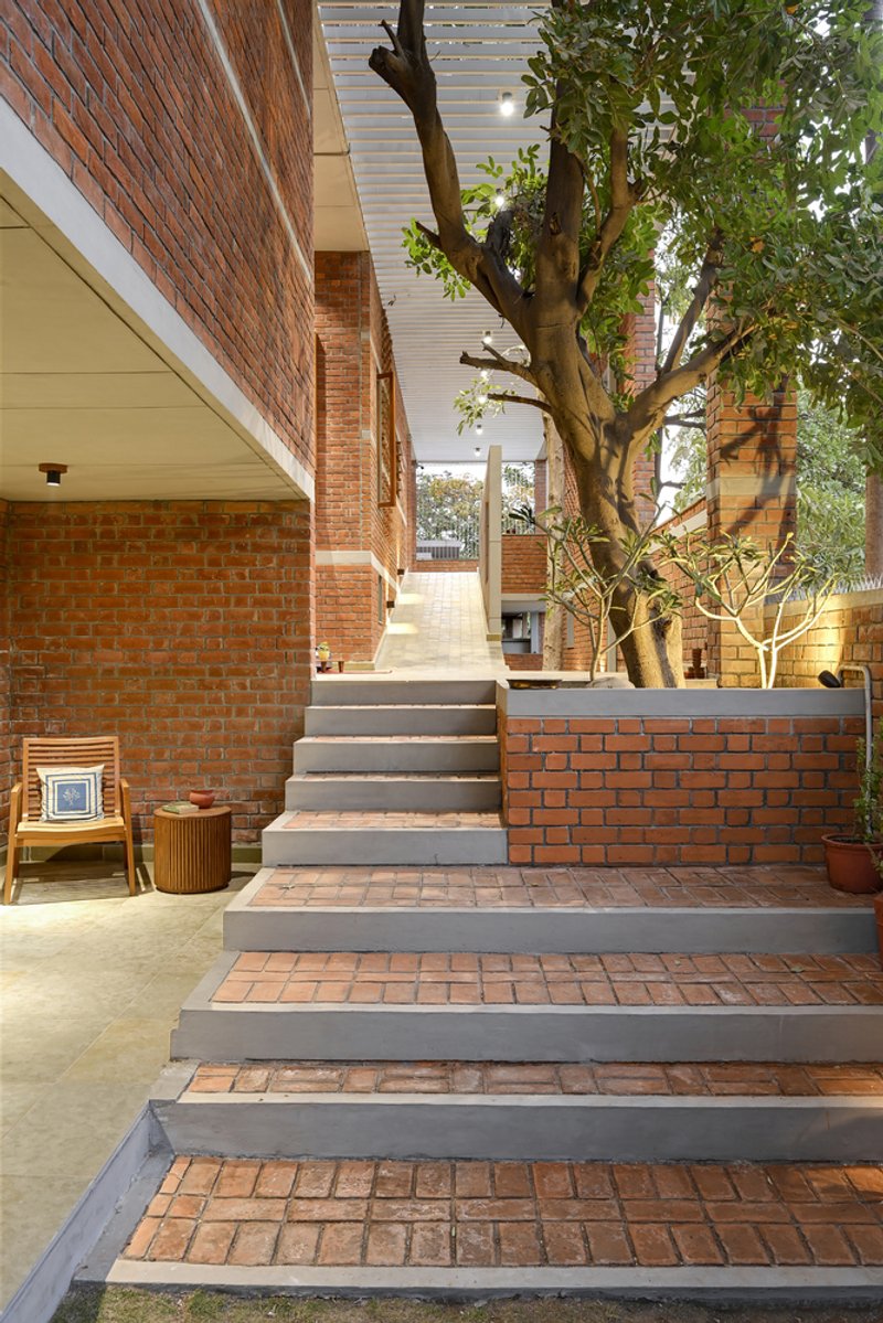 Outdoor staircase with brick treads and concrete risers ascending past a preserved tree in the courtyard