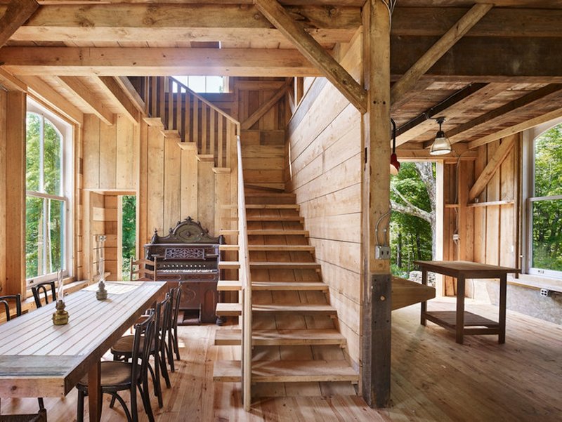 Central timber staircase rising between dining area and upper loft with exposed joists overhead