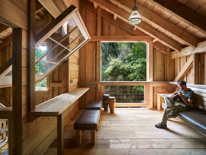 Upper-level nook with built-in bench seating and large window overlooking dense summer foliage