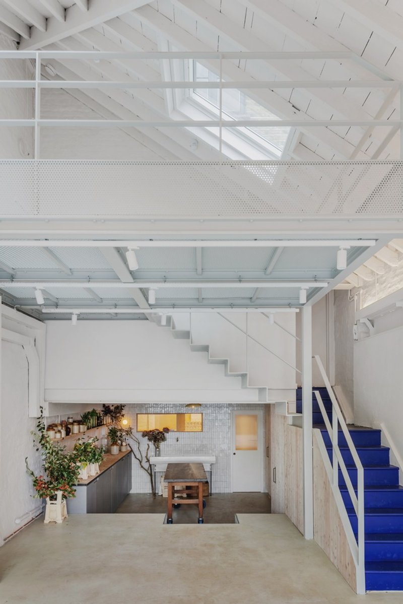 Double-height space showing mezzanine with perforated metal panels and blue staircase below