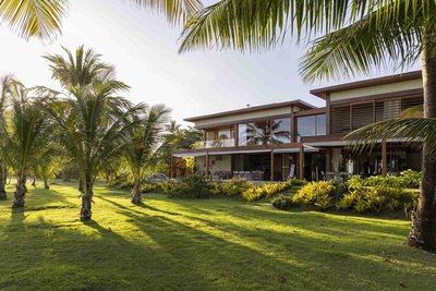 This architectural image showcases a modern, two-story house with a tropical design. The house featu