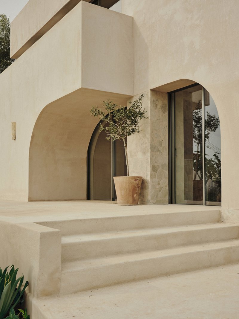 Arched passageway and terrace with potted olive tree and glazed doors under an overcast sky