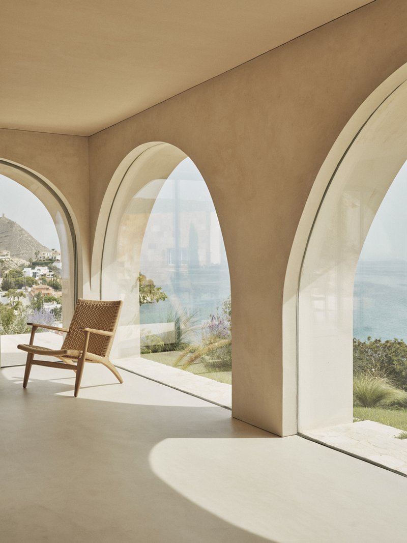 Interior loggia with vaulted arched openings and a woven lounge chair overlooking the coastal hillside