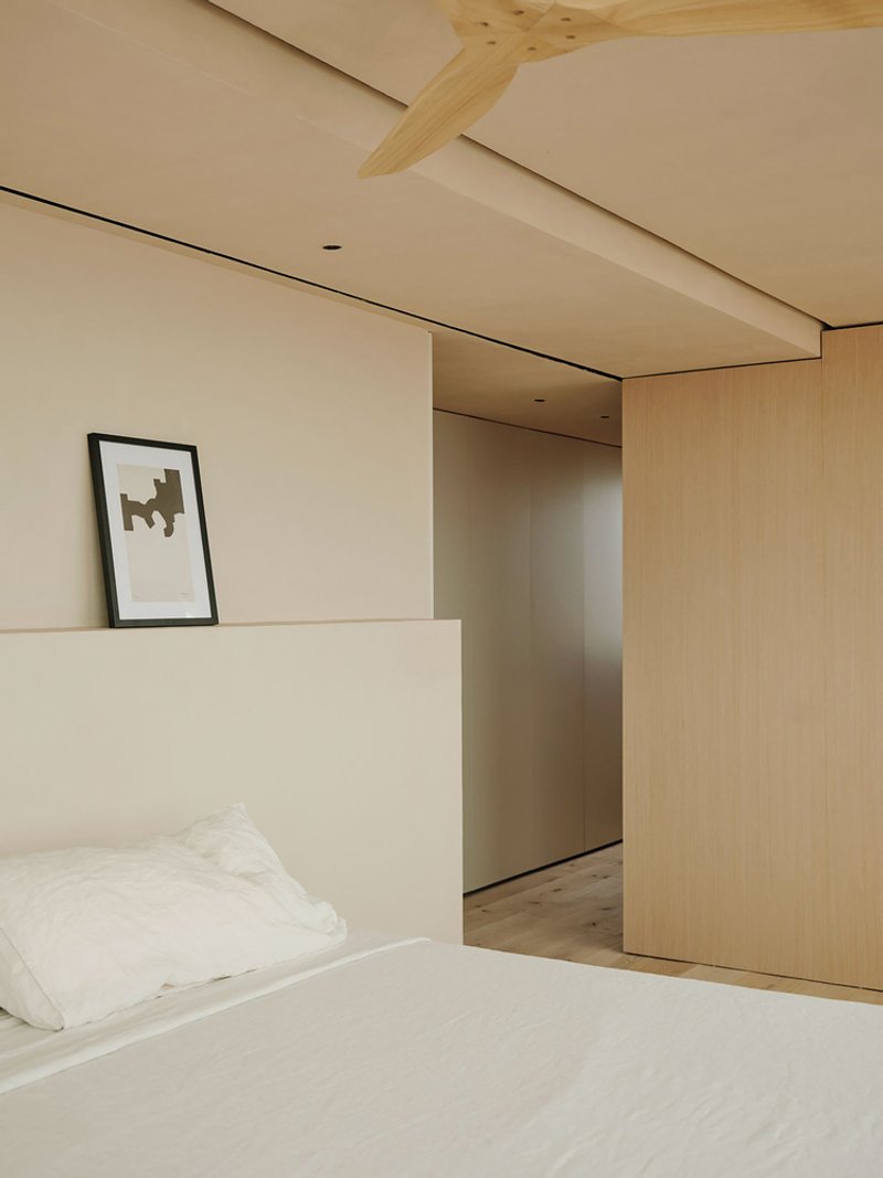 Bedroom with exposed timber beam crossing plaster ceiling above sliding wood partition and framed artwork