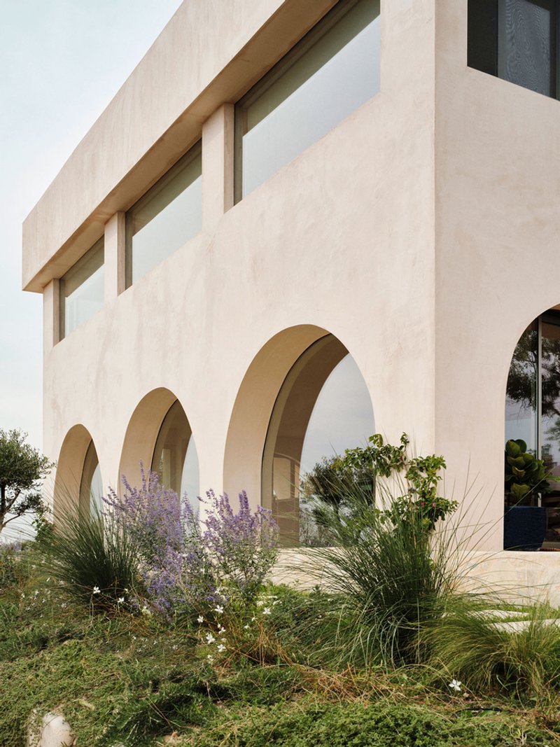Exterior view of stuccoed facade with three arched openings and planted beds of lavender and grasses