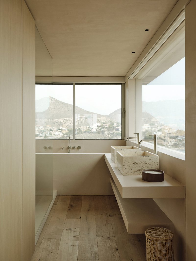 Bathroom with corner windows framing mountain views and travertine basin on floating vanity shelf