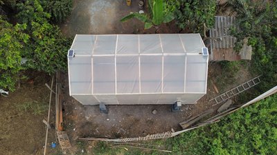 This aerial photograph showcases a greenhouse structure in a rural setting. The greenhouse features 