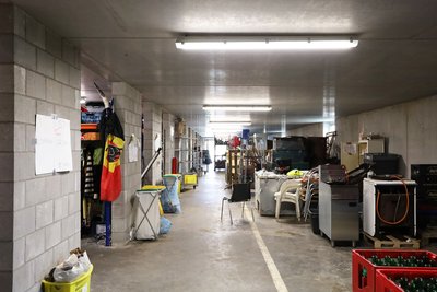 This photo depicts a long, cluttered corridor in what appears to be a storage area or warehouse. The