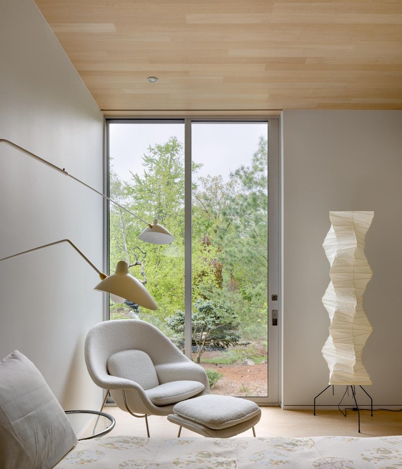 Seating area with floor-to-ceiling window overlooking garden and wood ceiling plane above white walls