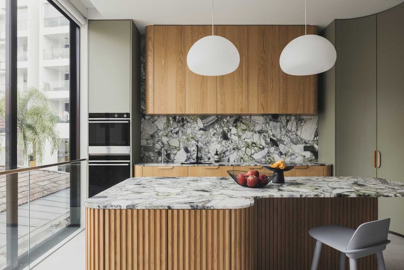 Kitchen island with veined marble top, timber-battened base and white globe pendants overhead