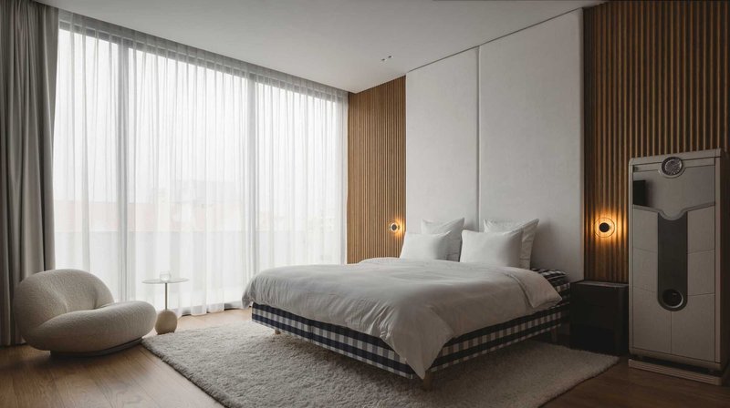 Bedroom with upholstered headboard wall, timber slat panels and sheer curtains filtering daylight