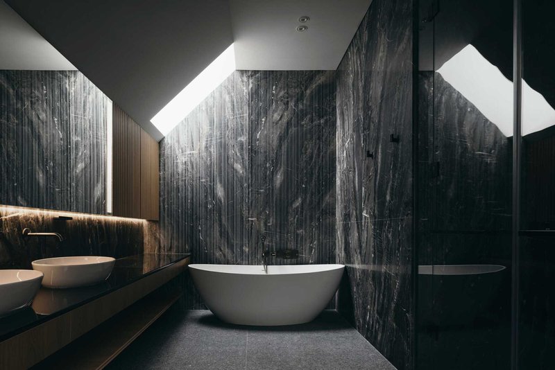 Bathroom interior with freestanding tub against dark marble walls lit by angular skylights above