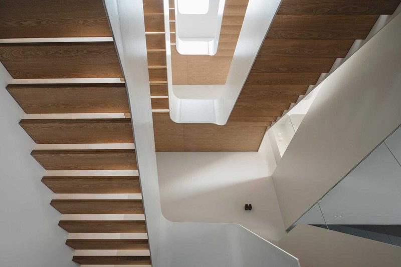 Upward view of timber staircase with glass balustrade beneath a coffered wooden ceiling with skylights
