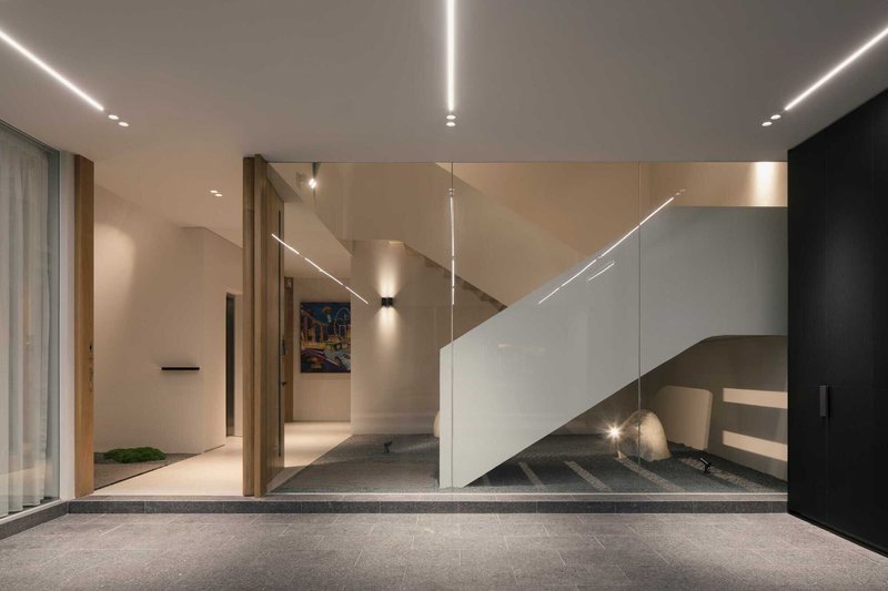 Entry foyer with white sculptural staircase and linear ceiling lighting in the evening