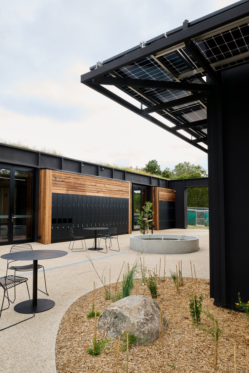 Courtyard detail with solar PV canopy overhead, timber locker wall and a round concrete water feature