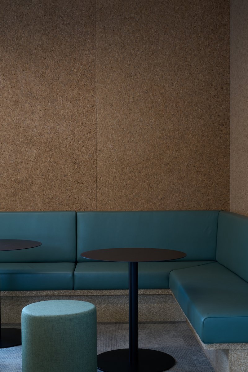 Close detail of the cork wall, teal leather banquette and round black tables