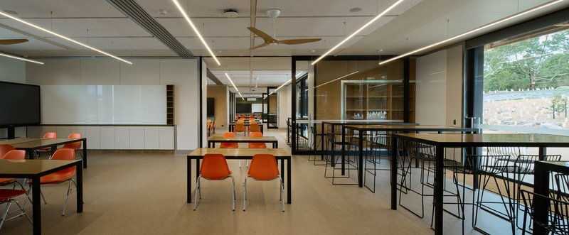 Long flexible classroom with whiteboards, orange moulded chairs, ceiling fans and a curtain wall to the garden
