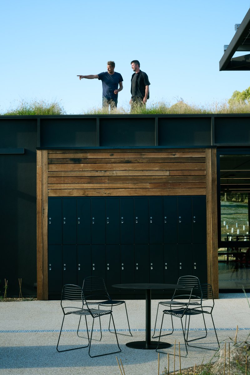 Two people on the green roof above the timber locker wall with students seated on the courtyard below