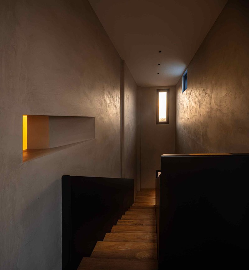 Narrow stairwell with black metal sides, timber treads and narrow window slits creating dramatic light patterns