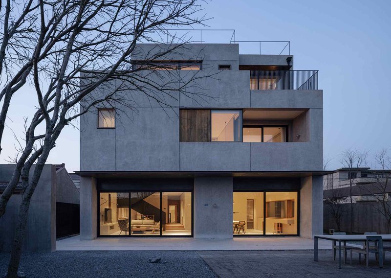 Rear elevation with large glazed openings and cantilevered terraces against a gravel courtyard at twilight