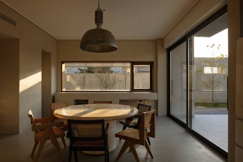 Dining room with round timber table beneath metal pendant and horizontal window facing the courtyard