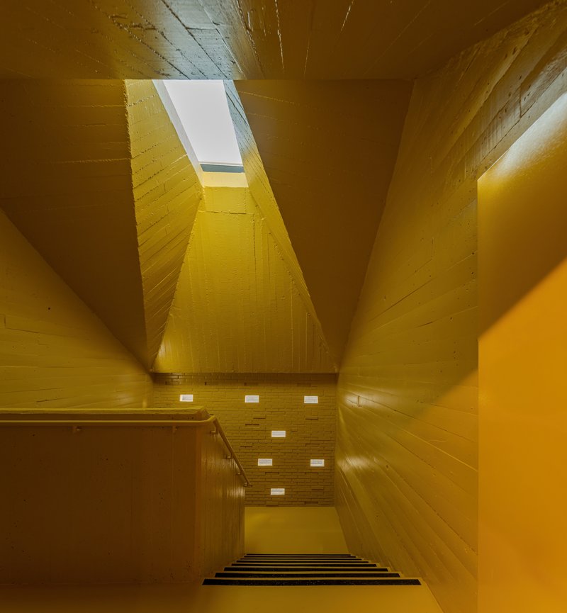 Looking up through a yellow-painted timber stairwell with a rectangular skylight at the top