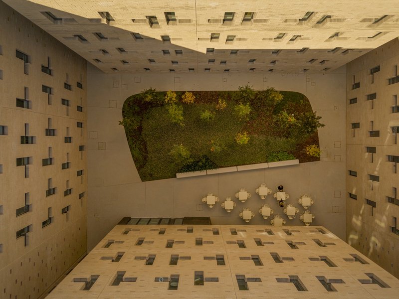 Aerial view into a courtyard with a vegetated wall, patterned paving, and small white tables below