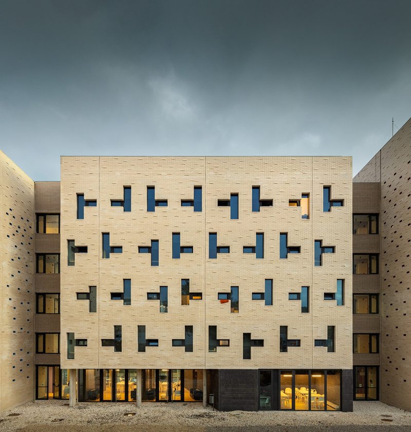 Courtyard facade with buff brick and irregular window openings under overcast skies