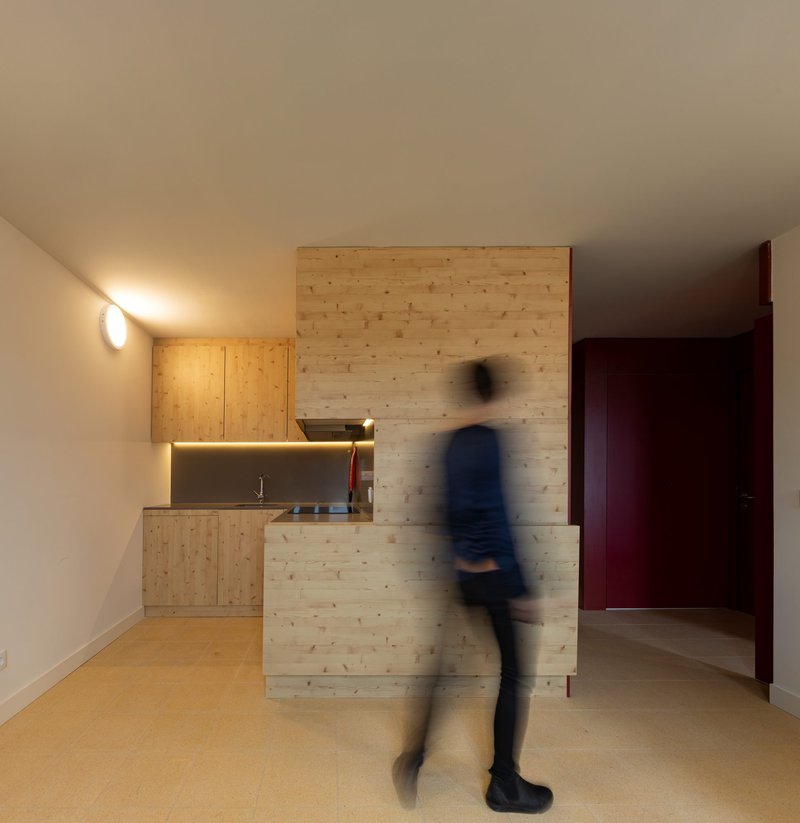 Compact kitchenette with timber cabinetry and a blurred figure in motion