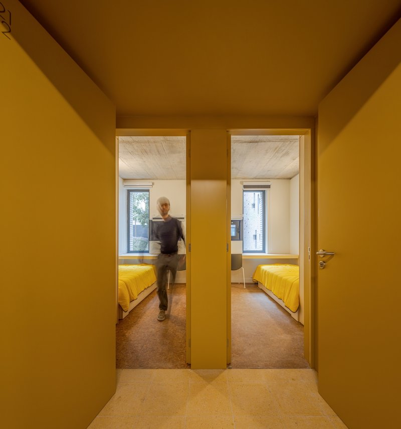 Mustard hallway looking through two doorways into bedrooms with yellow bedding and a person passing through