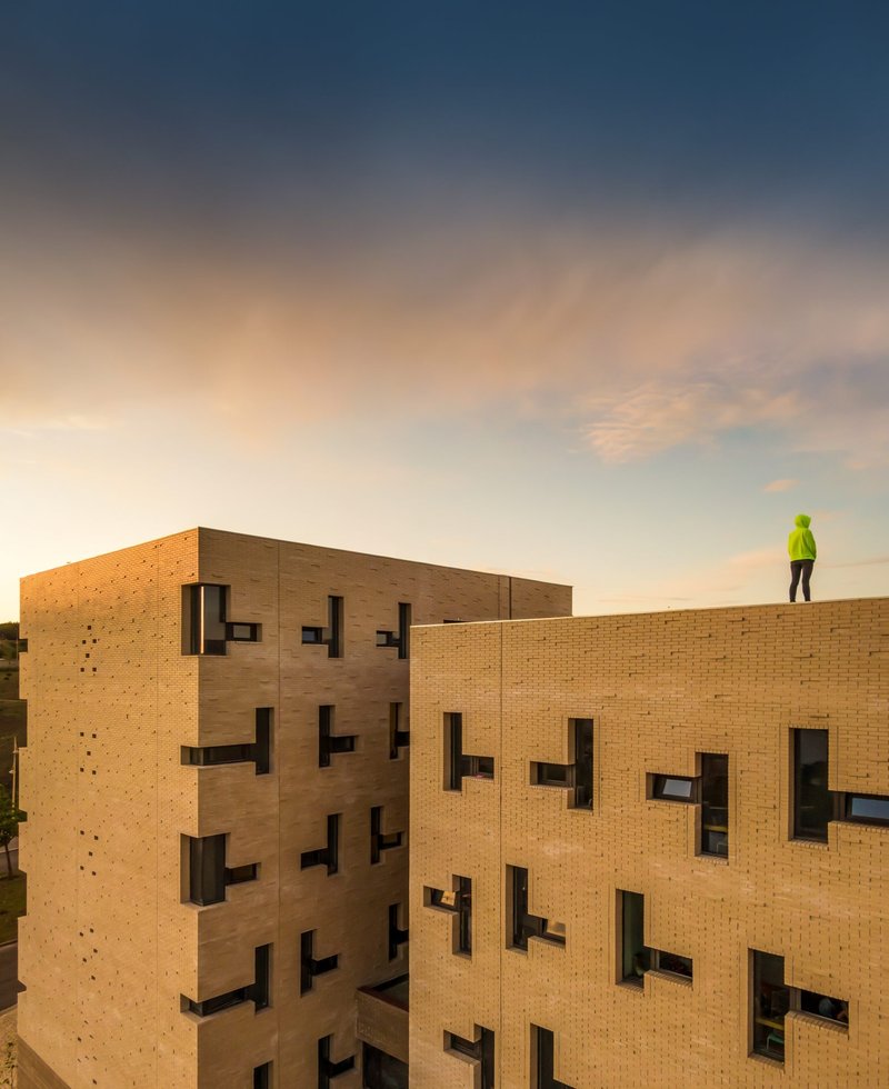 Brick facade with staggered window openings and a worker in high-visibility vest on the roof at dusk