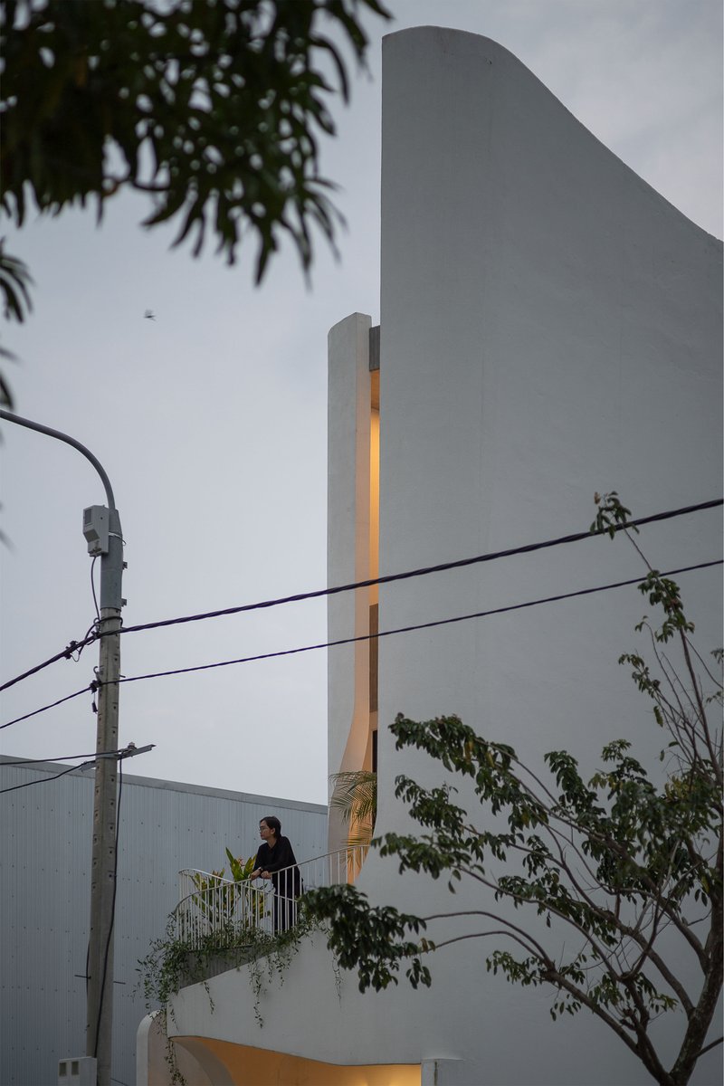 Dusk view of the white facade with illuminated vertical slot and figure on balcony