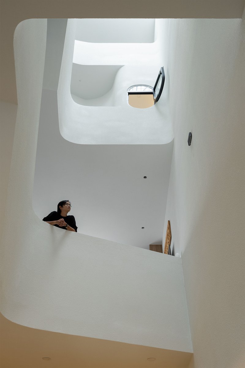 Vertical view of white stairwell with curved openings and person leaning over upper landing