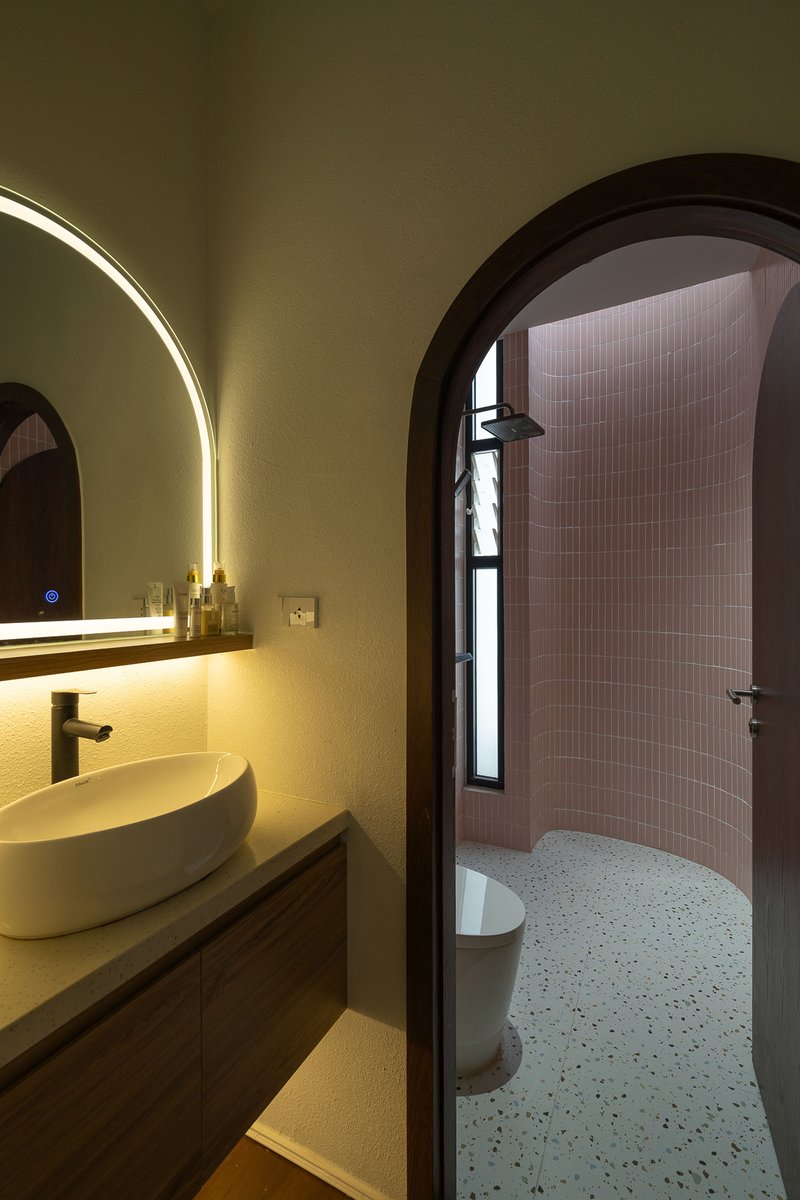 Arched bathroom entry revealing pink tiled shower enclosure and backlit circular mirror above vessel sink