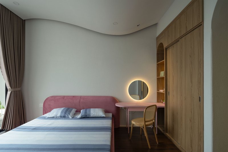 Bedroom with pink upholstered bed and integrated timber desk beneath curtained window in soft daylight