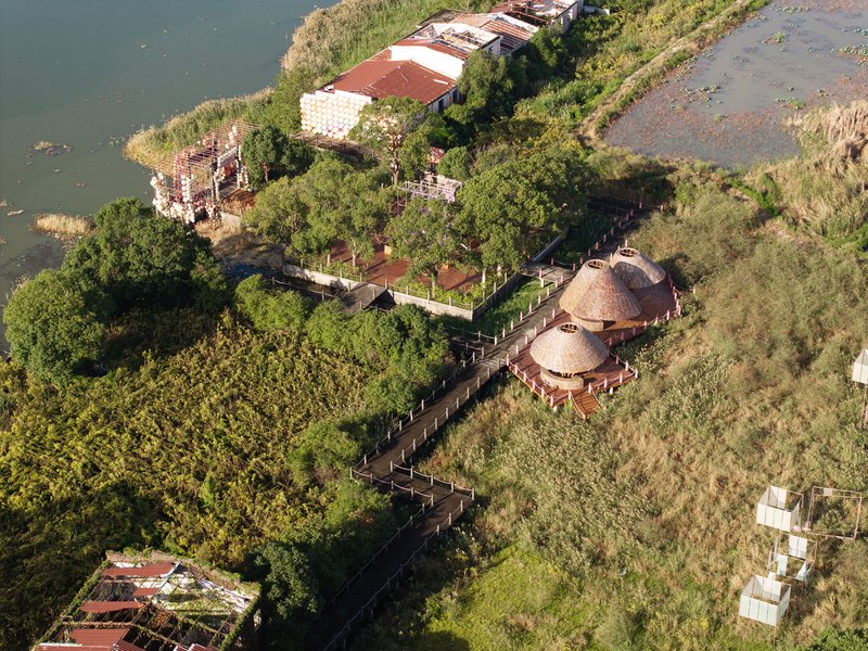 Drone view of woven bamboo pavilions connected by elevated boardwalks winding through planted beds and water