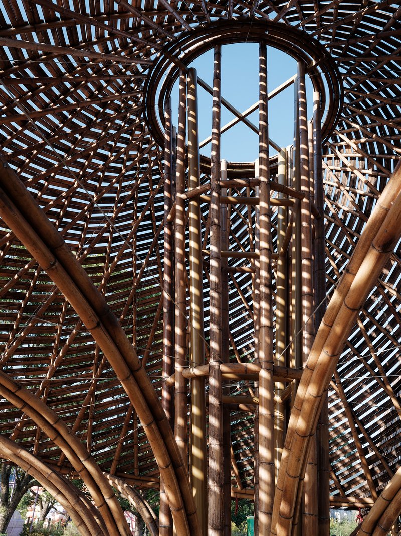 Interior view looking up through bundled bamboo columns and latticed roof structure to a circular oculus