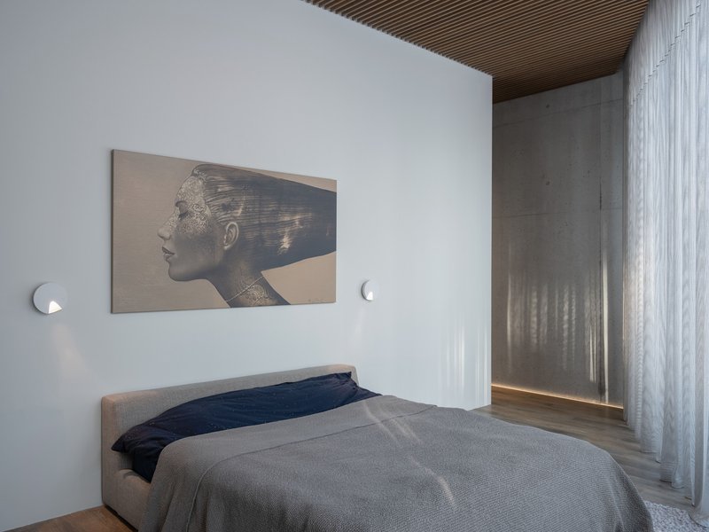 Bedroom with white walls, timber slat ceiling, and sheer curtains flanking a concrete panel