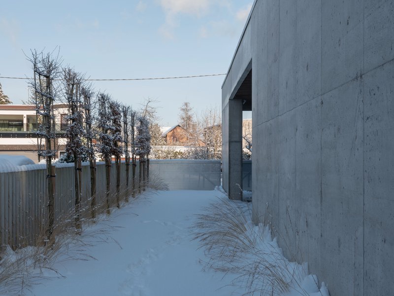 Concrete wall with recessed entrance alongside a snow-covered path and timber fence in winter